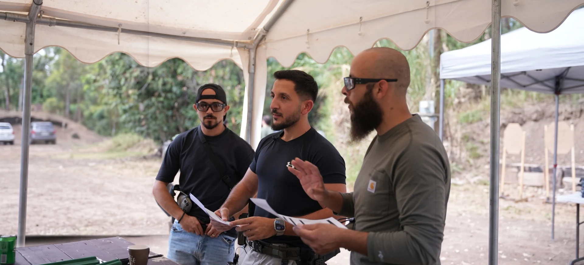 NES instructors briefing trainees under a tent at the range, plan pages in hand